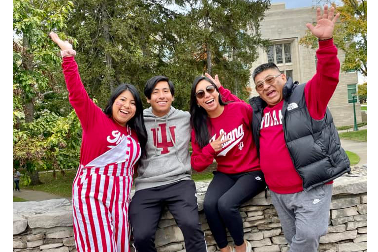 Four people dressed in various IU spirit wear smile while posing for a photo on the IU Bloomington campus.