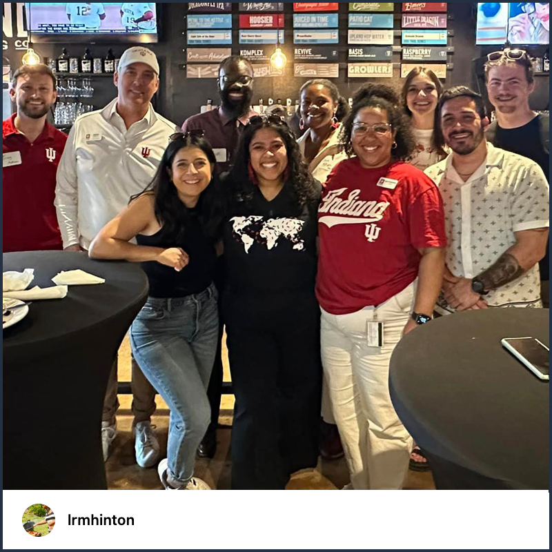 A group of 10 IU alumni dressed in various spirit wear pose for a photo in a restaurant at an IU Alumni Association Central Indiana chapter event.