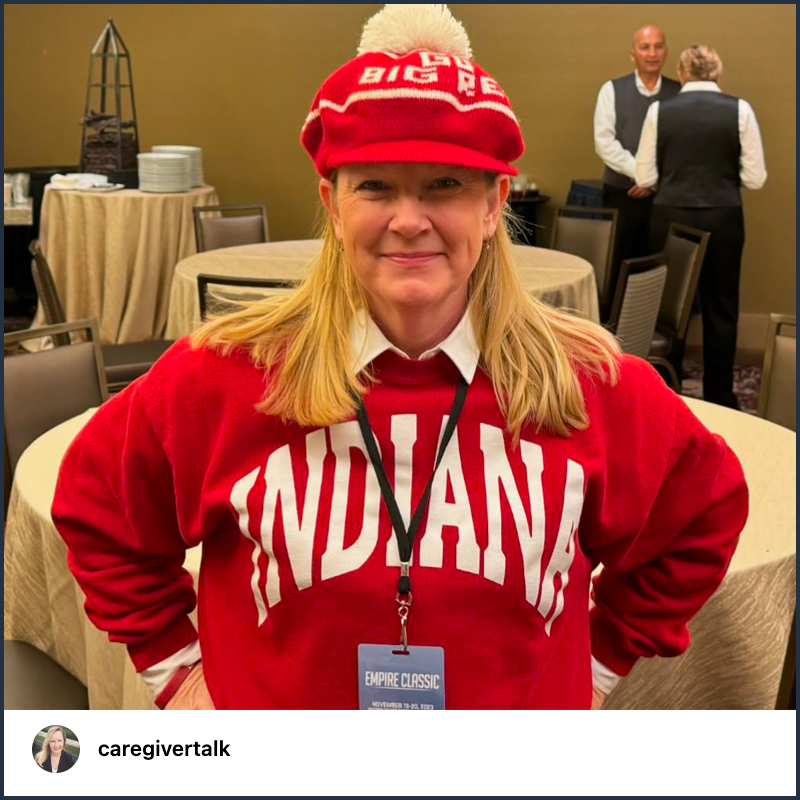 A woman, standing with her hands on her hips, smiles while wearing a red sweatshirt featuring the word “Indiana.” She also wears a red hat embroidered with the words “Go Big Red.”